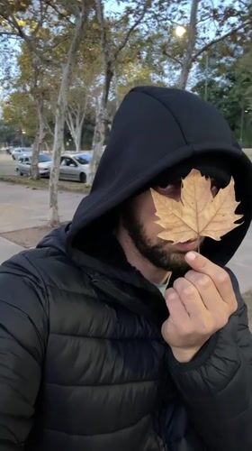 Man holds dried leaf over face on Buenos Aires sidewalk