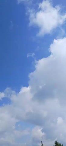 The video shows a bright blue sky with scattered white and gray clouds. The clouds are of various sizes and shapes, with some appearing wispy and others more dense. The overall impression is of a partly cloudy day with good visibility. There are no people or objects visible in the frame, and no discernible actions or interactions are taking place. The environment is purely the sky.
