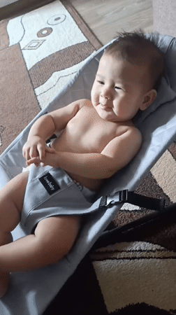 Baby in gray bouncer plays peek-a-boo with the camera