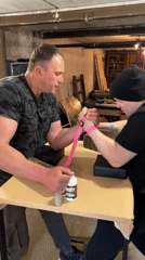 Two men arm wrestle with pink straps securing match