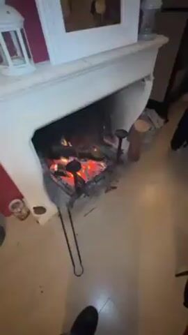 The video shows a fireplace with a fire, then pans out to show a group of people sitting on couches. A group of people plays pool. The room has stone walls.