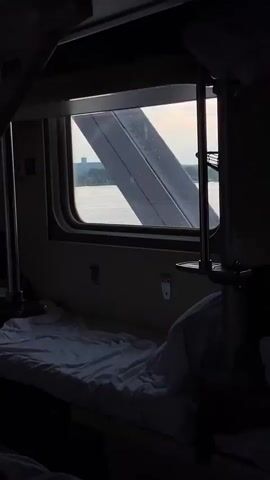 The video shows the interior of a train compartment with a bed and a window. Through the window, a body of water and a distant cityscape are visible. The train is in motion, as evidenced by the changing view outside the window. The lighting is dim, suggesting either early morning or late evening. No people are visible in the frame.