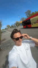 Man puts on sunglasses, smiles on Oslo sidewalk