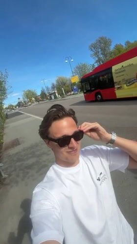 Man puts on sunglasses, smiles on Oslo sidewalk