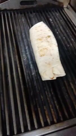 A person places a white wrap onto a black metal grill, gently pressing it down.