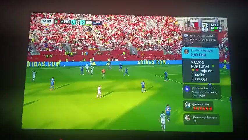 The video shows a screen displaying a soccer game. The score is 0-0, and the time is 20:55. The game is between Portugal and Croatia. The field is green, and there are many spectators in the stands, mostly wearing red. There are several players on the field wearing white and blue uniforms. On the right side of the screen, there is a live chat feed with user names and comments. The overall atmosphere appears to be that of a live sports broadcast.