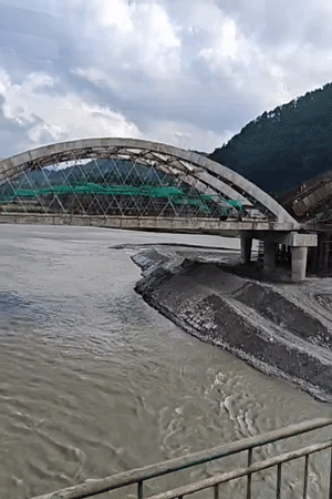 Arched bridge under construction spans muddy river in rural Nepal