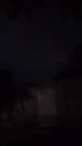 The video is dark and grainy, with the majority of the frames showing a black screen. There are brief moments where faint objects are visible. In one frame, there appears to be a brick wall with a faint light shining on it. In another, a small red circle is visible against a dark background, possibly a light or reflection. The final frames show a blurry, dark landscape with hints of purple light in the distance, suggesting lightning. The footage is of poor quality and lacks clear details.