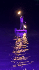 Fire performer demonstrates torch juggling on water platform in Thailand