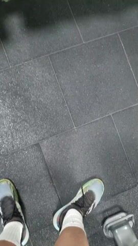 The video shows a rack of black dumbbells in a gym. The dumbbells are arranged in three rows, with each pair marked with its weight. The rack is a vibrant yellow. In the background, gym equipment and a person in a red shirt and shorts are visible. The camera zooms in on the rack of dumbbells.