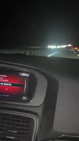 The video, taken from the inside of a car, shows a dark highway at night. Several car headlights are visible in the distance. The car's dashboard is visible, displaying a speed of 200 km/h and a temperature of 20.6 degrees Celsius. Music is playing in the background.