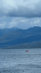 Red motorboat carries passengers across Indonesian waters near mountains