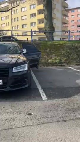 A low-angle shot captures a black Audi S8 parked on asphalt, angled slightly to the left. The driver's side door is ajar, with a person exiting.  The vehicle's Bulgarian license plate, "CB 9991 TH," is visible. The background includes a light yellow apartment building, a curb, and a tree. Sunlight is apparent, suggesting a daytime scene.