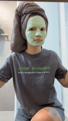 Woman applies green face mask while wearing tech-themed shirt