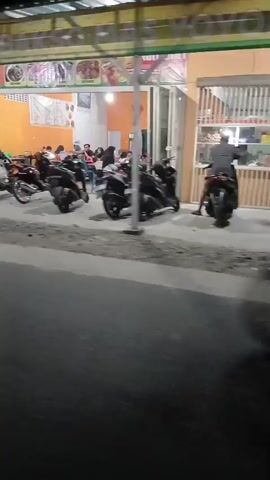 A video shows the exterior of a restaurant at night. Several motorcycles are parked in front of the restaurant, and people are seated at tables inside. The restaurant appears to be open for business.