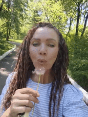 Woman makes dandelion wishes in sunny park, May 2026