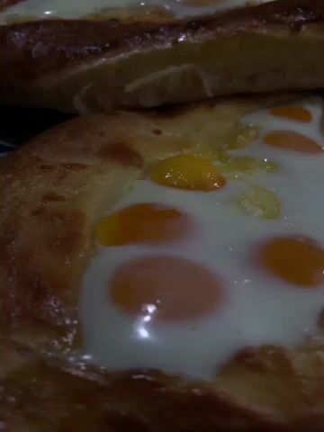 The video displays a close-up view of several baked goods, likely pastries, arranged in layers. The pastries appear to be filled with a creamy white substance and have visible egg yolks scattered throughout, some appearing cooked and others less so. The crust of the pastries is golden brown and appears slightly flaky. The lighting is warm and suggests an indoor setting, possibly a kitchen or bakery. The camera pans slowly, offering different angles of the food.