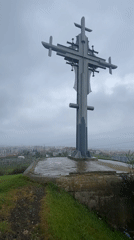 Metal cross monument overlooks Burgas cityscape under overcast skies