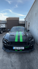 Modified black Mustang with racing stripes parked in outdoor lot