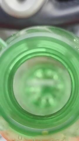 A close-up, downward-facing shot of the inside of a green plastic bottle. The bottle opening is in focus, revealing concentric ridges around the rim. The interior of the bottle is blurred, but the bottom is visible with a star-like pattern, suggesting it is a typical plastic bottle base. The lighting is bright, casting a slight glare on the plastic.