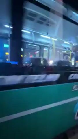 The video shows a green and white city bus, number 17 and labeled 224, traveling on a city street at night. The video is shot from the perspective of another vehicle moving alongside and then behind the bus.  The bus has visible passengers inside. Streetlights and building lights illuminate the scene. Cars are visible driving nearby. The bus has multiple taillights and turn signals. The number "60" is displayed in a circle above the bus's rear window. The bus's license plate is partially visible. The surroundings indicate a dense urban environment.
