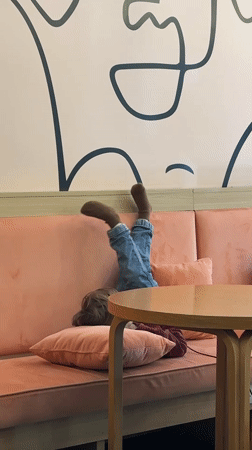 Child rests playfully on cafe sofa in Novi Sad
