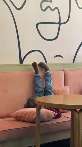 Child rests playfully on cafe sofa in Novi Sad