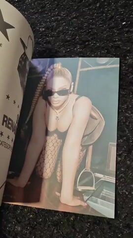 A hand flips through the pages of a large photo book on a black, textured surface. The book features various stylized photographs of people, including one of a woman in fishnet stockings and sunglasses kneeling, and others showing figures in diverse, artistic settings and poses. Some photos are full of color and light, while others are more dimly lit. The pages also contain text, such as "Club Renaissance - October 2022 PARIS, FRANCE". The hand moves quickly to show the variety of photos within the book.