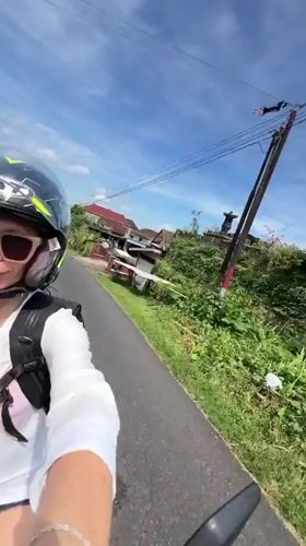 Woman on motorcycle smiles while riding through Pupuan, Indonesia