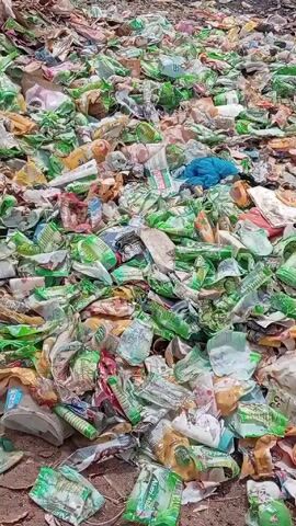 The video shows a large amount of litter scattered across a ground of dirt and gravel. The litter consists of plastic wrappers, bottles, and bags, predominantly in shades of green, white, and yellow. Some items are crumpled and torn. A small piece of blue fabric is also visible among the waste. The ground is uneven, and some litter is partly obscured by other pieces.