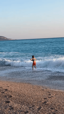 Children play on Fethiye beach amid paragliding activity