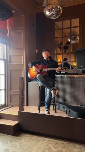 Acoustic guitarist performs on wooden platform in Dundee venue