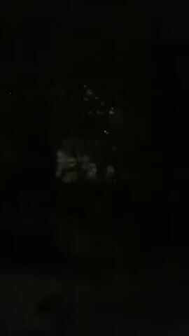 The video starts with a dark, grainy view of an unclear exterior scene with some light sources. It then transitions abruptly to an interior shot of a train. The interior is visible as the camera moves quickly along the train's interior wall, showing the windows and the doors leading to other cars. The walls are painted a yellow color, and there are silver metal bars and window frames. The doors are orange. The video ends before anything else is clearly visible.