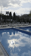 Empty pool reflects cloudy sky on bright afternoon
