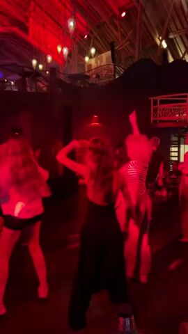 The video captures a lively indoor scene, likely a party or club, bathed in vibrant red lighting. Several individuals are seen dancing, their movements suggesting a celebratory atmosphere. The setting appears to be a large room with a high, rustic ceiling, possibly made of wood beams. Hanging lights and what looks like a DJ booth with equipment are visible, reinforcing the idea of a music-driven event.

The subjects are primarily young adults, dressed casually for dancing. They are engrossed in their activity, with some looking towards the DJ or the general party space. The red lighting creates a dynamic and energetic mood, perhaps masking specific details about the time of day or weather, which are not discernible from the footage. The location cues, such as the architecture and the presence of a DJ, suggest an entertainment venue. The overall emotion conveyed is one of fun and engagement with the music and social gathering. No visible text is present in the frames. The scene is consistent with a night-time party in a venue in Kediri, Indonesia.