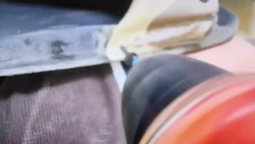 A close-up shot shows a person using a drill to insert a screw into a boot. The drill bit is blue and the screw is black. The boot appears to be made of leather and fabric. The background is blurred, but suggests an indoor setting with a brown textured surface.