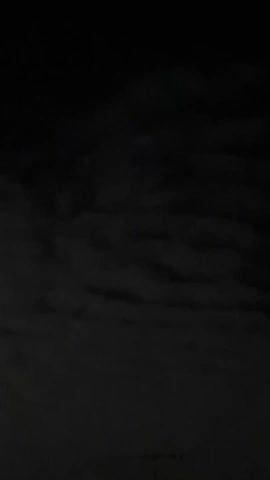 The video shows a night sky with a full moon. The moon is partially obscured by clouds, which create a halo effect around it. The sky is dark, and the clouds are a mixture of gray and white. The video is handheld and shaky. There are faint sounds of traffic in the background.