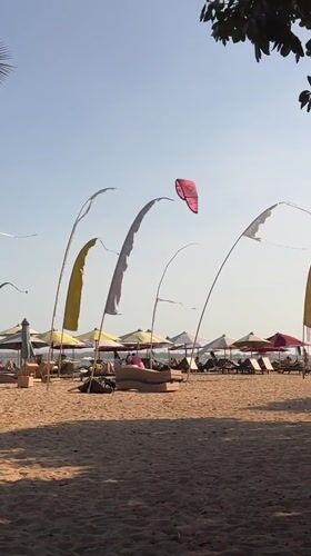 Kites, kitesurfers, and ceremony flags on a Bali beach