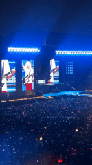 Large arena concert features guitarist, red lighting, packed crowds