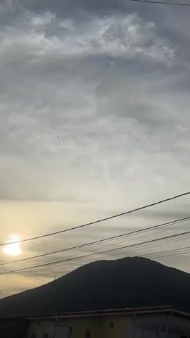 A vertical video opens on a dusky sky with clouds and power lines. Two mountains appear in the background, silhouetted against the sky. As the video progresses, the sky becomes brighter, revealing a clear blue sky interspersed with clouds. Power lines continue to stretch across the frame. A street lamp is visible in the upper left quadrant of the frame. The video ends on the same mountainous landscape and sky, with more clouds visible.