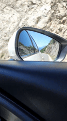 Vehicle travels scenic coastal road past cliffs and wildflowers