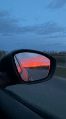 Motorist captures vivid sunrise reflected in rainy car mirror