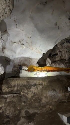 Woman meditates at cave temple with reclining Buddha statue