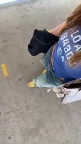 A woman wearing roller skates, blue jeans with holes in them, and a blue t-shirt is squatting on a concrete surface. She has a black jacket draped over her lap and a white purse sitting near her feet. A shiny metal object moves past her on the left. The camera is positioned above the woman, looking down.