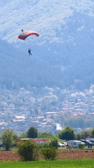 Parachutist descends over Bulgarian countryside as aircraft flies overhead