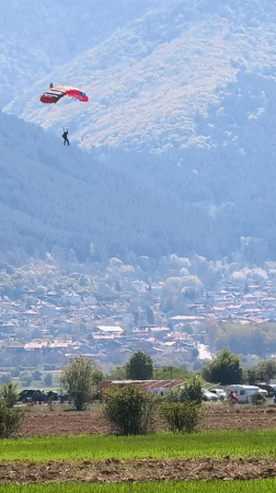 Parachutist descends over Bulgarian countryside as aircraft flies overhead