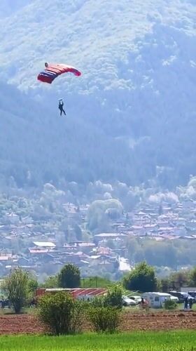 Parachutist descends over Bulgarian countryside as aircraft flies overhead
