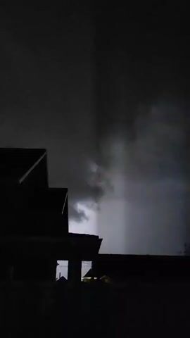 This is a video file capturing a nighttime scene in Dinskaya, Russia. The predominant subject is darkness, with very little light visible. In the lower portion of the frame, there is a faint suggestion of a building or structure, possibly with some illuminated windows or lights from a street or vehicle. A thin horizontal line of light can be seen, hinting at a road or a low-lying light source. The sky is completely black, indicating it is nighttime, and there is no indication of clear weather conditions, as the darkness obscures any celestial bodies or atmospheric phenomena. The overall impression is one of a quiet, dimly lit, and possibly deserted urban or suburban environment. No people are directly visible, and the only identifiable objects are the faint outlines of structures and artificial lights. The time of day is clearly night, and the weather is dark and likely overcast or devoid of ambient light. No text is visible in the frame.