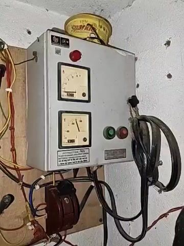 The video shows an electrical panel mounted on a wall. It contains multiple components including a main switch, meters, circuit breakers, and electrical outlets. The wiring appears to be exposed and somewhat disorganized. The panel is made of metal and is attached to a wooden board. There are also some plastic conduits and cables running along the wall. A yellow object with "Spark" written on it is placed on top of the electrical panel.