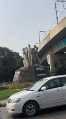 Morning traffic flows past family statue in Dhaka